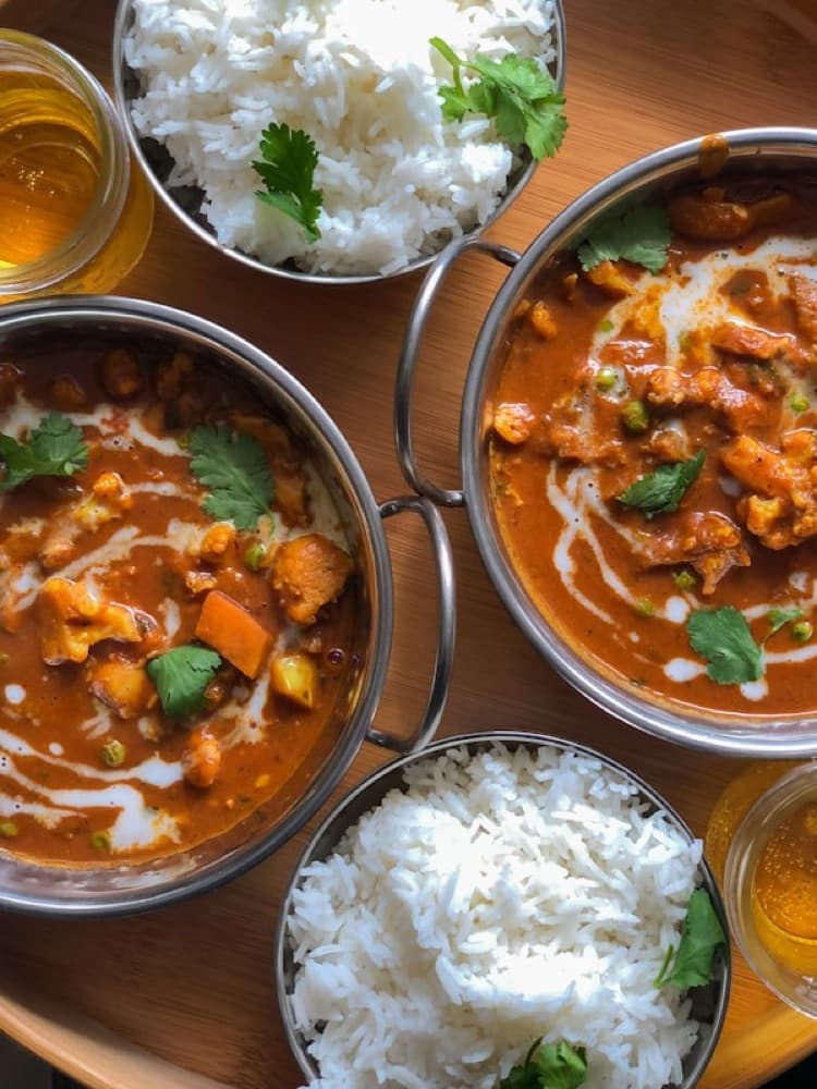 Overhead shot of two copper kadai bowls with curry alongside steaming basmati rice