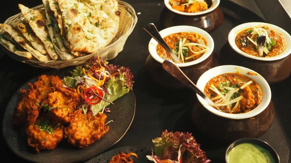 Three bowls of Indian curry served with naan and pakoras